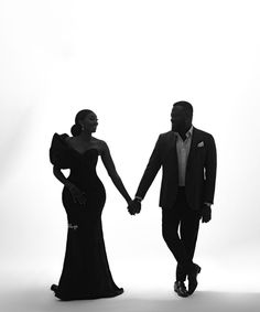 a black and white photo of a man and woman in formal wear walking hand in hand