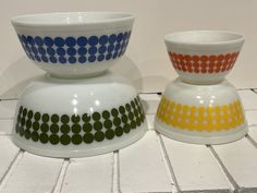 two colorful bowls sitting on top of a white tiled floor next to each other in front of a wall