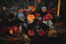 an arrangement of flowers on a table with candles and scarves in the dark background