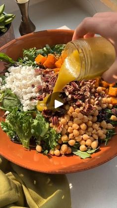 a person pouring dressing onto a salad in a bowl with greens and chickpeas