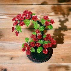 a small vase with red flowers and green leaves on a wooden surface, sitting on a table