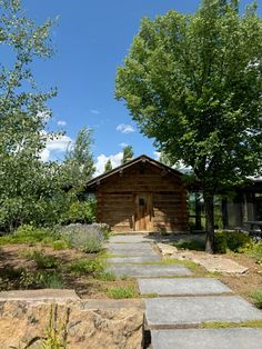 a wooden cabin sitting in the middle of a lush green forest next to a stone walkway