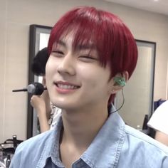 a young man with red hair and piercings smiles at the camera in front of a mirror