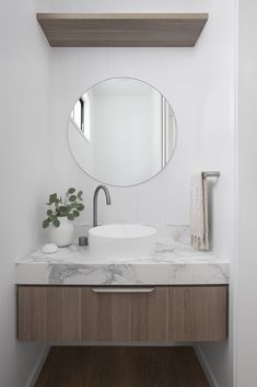 a bathroom vanity with a round mirror above it and a plant on the counter top