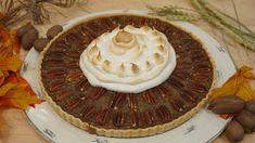 a pecan pie with whipped cream on top sits on a plate surrounded by autumn leaves