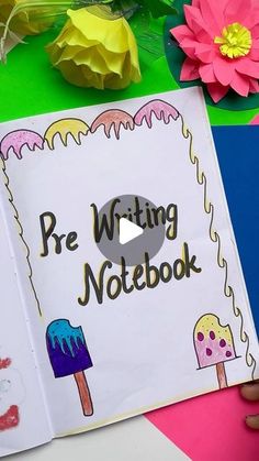 an open notebook with writing on it and paper flowers in the background next to it