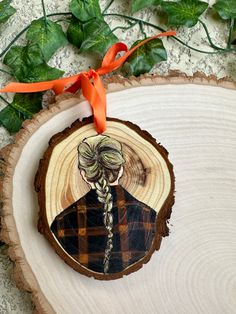 a wooden ornament with a woman's face painted on it and an orange ribbon