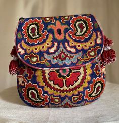 "Medium size Flat Silk Petit Point Handbag created and handmade in Uzbekistan. Lined with silk and cotton ikat fabric, hand woven silk straps and tassels and a magnetic snap closure. Each handbag is hand drawn onto cotton canvas, inspired by original designs from Uzbekistan textile history.  8.25\" high x 8.25\" width, top opening 6\" wide approx. 64\" strap x 1/2\" width.  Can fit largest sizes of iPhone and Android. 100% silk petit point with handwoven silk and cotton ikat lining. The strap is Handmade Multicolor Folk Bags, Traditional Blue Handwoven Shoulder Bag, Traditional Blue Handwoven Bags, Traditional Blue Woven Shoulder Bag, Traditional Blue Woven Bag, Traditional Multicolor Pouch Shoulder Bag, Handmade Multicolor Tapestry Shoulder Bag, Handmade Multicolor Tapestry Bags, Bohemian Embroidered Tapestry Bags