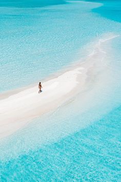 an aerial view of a person walking on the sand bar in the middle of the ocean