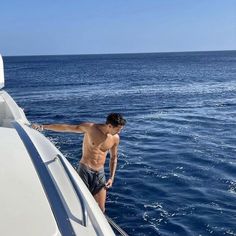 a shirtless man standing on the bow of a boat in the open water,