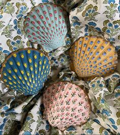 four decorative seashells sitting on top of a flowered cloth covered tablecloth