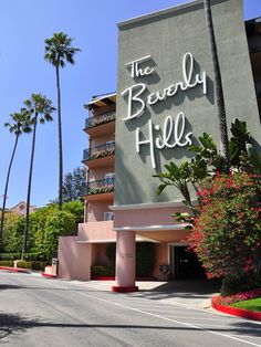 the beverly hills hotel sign is shown in front of palm trees and bushes on a sunny day