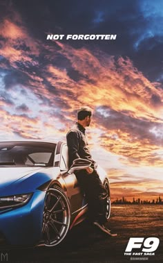 a man sitting on top of a blue car next to a sky filled with clouds