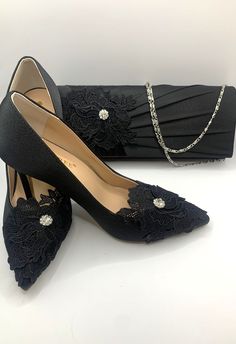 a pair of black high heeled shoes next to a clutch bag on a white surface