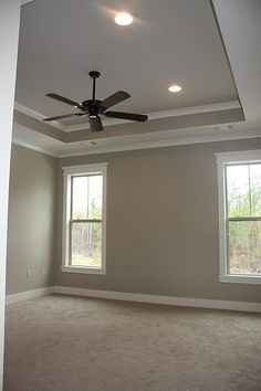 an empty room with two windows and a ceiling fan in the middle of the room