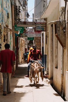 a man riding on the back of a cow down a street next to people walking