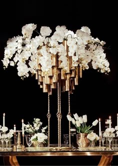 a table topped with lots of white flowers next to tall gold candles and vases