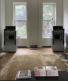 a living room with two large windows and a rug on the floor in front of it