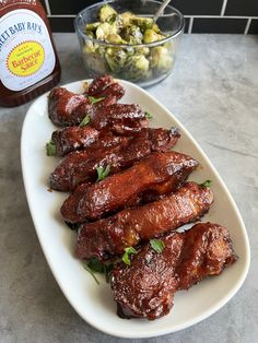 some meat on a white plate next to a bottle of beer