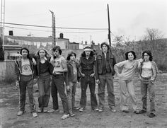 a group of people standing next to each other on a dirt road in front of buildings