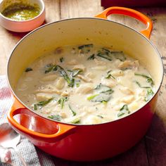 a red pot filled with chicken and spinach soup on top of a wooden table