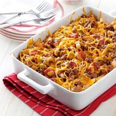 a casserole dish with meat and cheese in it on a red napkin next to silverware