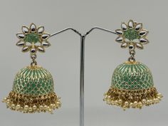 Immerse yourself in the exquisite charm of these Green and Gold Jhumka Earrings, meticulously handcrafted to reflect the rich cultural heritage of India. These stunning earrings feature a beautiful floral design at the top, leading to a gracefully patterned dome in green and gold. The intricate lattice work on the dome is accentuated with delicate pearls hanging elegantly, adding a touch of sophistication and grace. Gold Jhumka Earrings, Heritage Jewellery, Indian Heritage, Jhumka Earrings, Stunning Earrings, Green And Gold, Jewelry Earrings Dangle, Floral Design, Dangle Drop Earrings