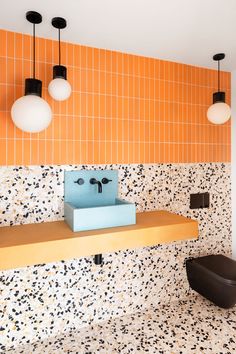 an orange and white tiled bathroom with a blue sink in the center, two hanging lights above it