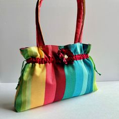 This adorable multicolored vertically striped shoulder bag is the perfect accessory to your summer outfit.  This medium sized purse fits a lot of your personal items and is quite spacious.  It is very sturdy as it is made out of a heavy cotton outer layer, a lightweight cotton inner layer and fusible fleece between the inner and outer layer.  Two drawstrings are added to the front and back channels and are pulled and tied together at the ends; giving the purse its shape.  The flower in the front Summer Rectangular Shoulder Bag With Striped Lining, Summer Tote Shoulder Bag With Striped Lining, Rainbow Bags For Everyday Summer Use, Rainbow Everyday Bags For Summer, Summer Shoulder Bag For Shopping With Striped Lining, Vibrant Multicolor Bags For Summer, Vibrant Multicolor Summer Bags, Multicolor Tote Bag With Striped Lining, Spring Travel Striped Shoulder Bag