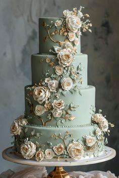 a three tiered blue wedding cake with white and gold flowers on the top layer