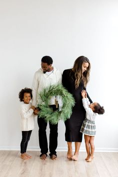 a family standing in front of a white wall holding a christmas wreath and two children