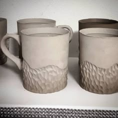 two white mugs sitting on top of a counter next to cups with lids and handles