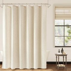 a white shower curtain in a bathroom next to a table with a towel on it