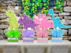 colorful paper dinosaurs are on display in front of a brick wall and green plants behind them