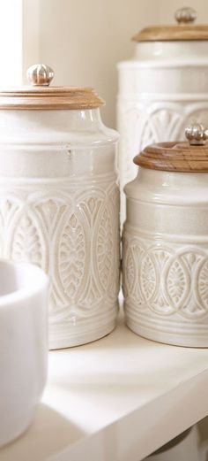 three white canisters sitting on top of a shelf next to a bowl and spoon