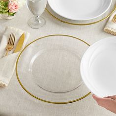 a person holding a white plate with gold trim around it on top of a table