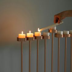 a person lighting candles in a row with one hand on the candle holder, while another is reaching for it