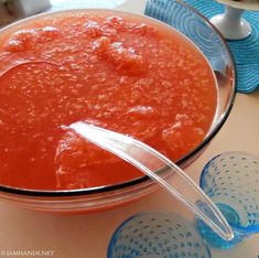 a bowl of tomato sauce with three glasses on the table next to it and a spoon