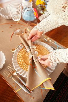 a person is setting a table with gold plates and silverware on it, while wearing lace gloves