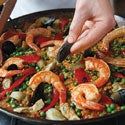 a pan filled with shrimp and vegetables on top of a stove next to a pair of tongs