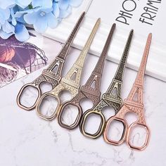 four pairs of scissors with the eiffel tower on them sitting next to blue flowers