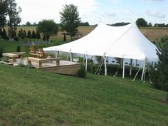 a large white tent set up in the middle of a field with tables and chairs under it