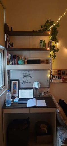 a desk with a laptop and books on it in front of a window filled with lights