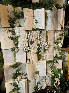 an arrangement of books with flowers and greenery on the wall behind them that says it's a love story