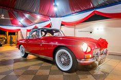 an old fashioned red car is parked in a room with white and red drapes