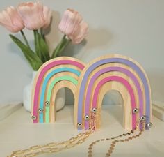 two wooden rainbows are on a table next to some flowers and a gold chain