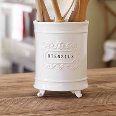 utensils in a white ceramic container on a wooden table with the word utensils printed on it