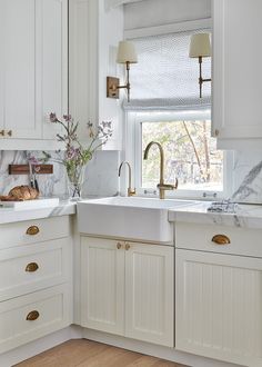 a kitchen with marble counter tops and white cabinets, along with gold pulls on the faucets