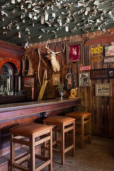 there are many deer heads hanging from the ceiling in this bar with two stools