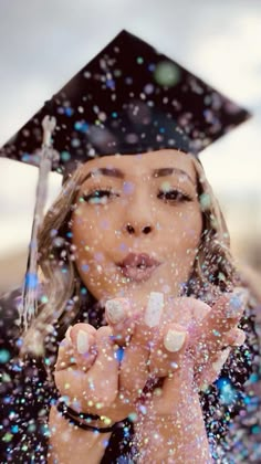 a woman wearing a graduation cap and gown blowing bubbles in front of her face while she holds